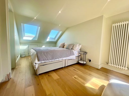 Loft conversion master suite bedroom Bright loft conversion minimalist bedroom with a large bed, slanted ceiling, and wooden floor. Ealing, London W13